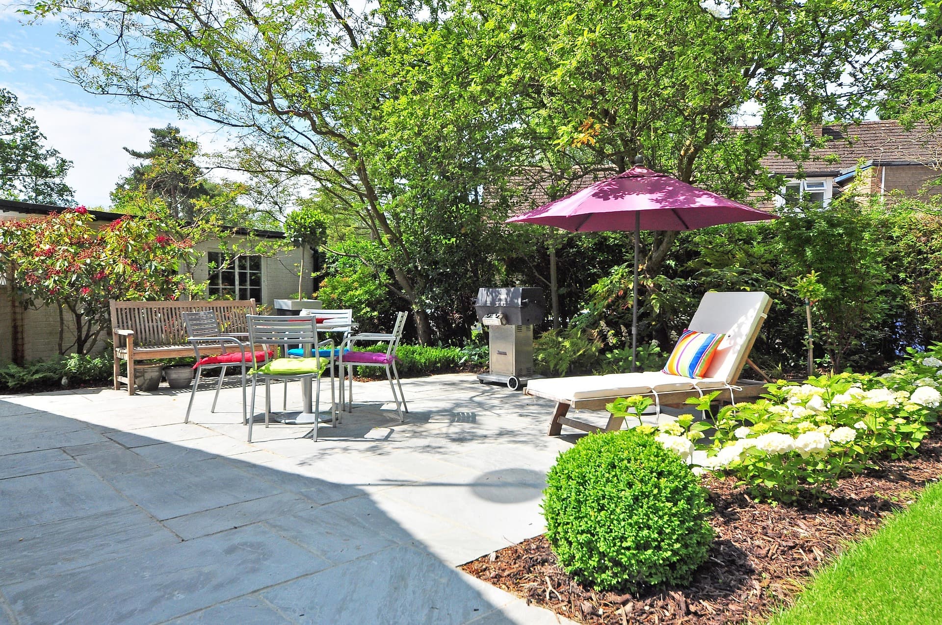 Terrasse dallée aménagée avec salon de jardin, parasol et massifs