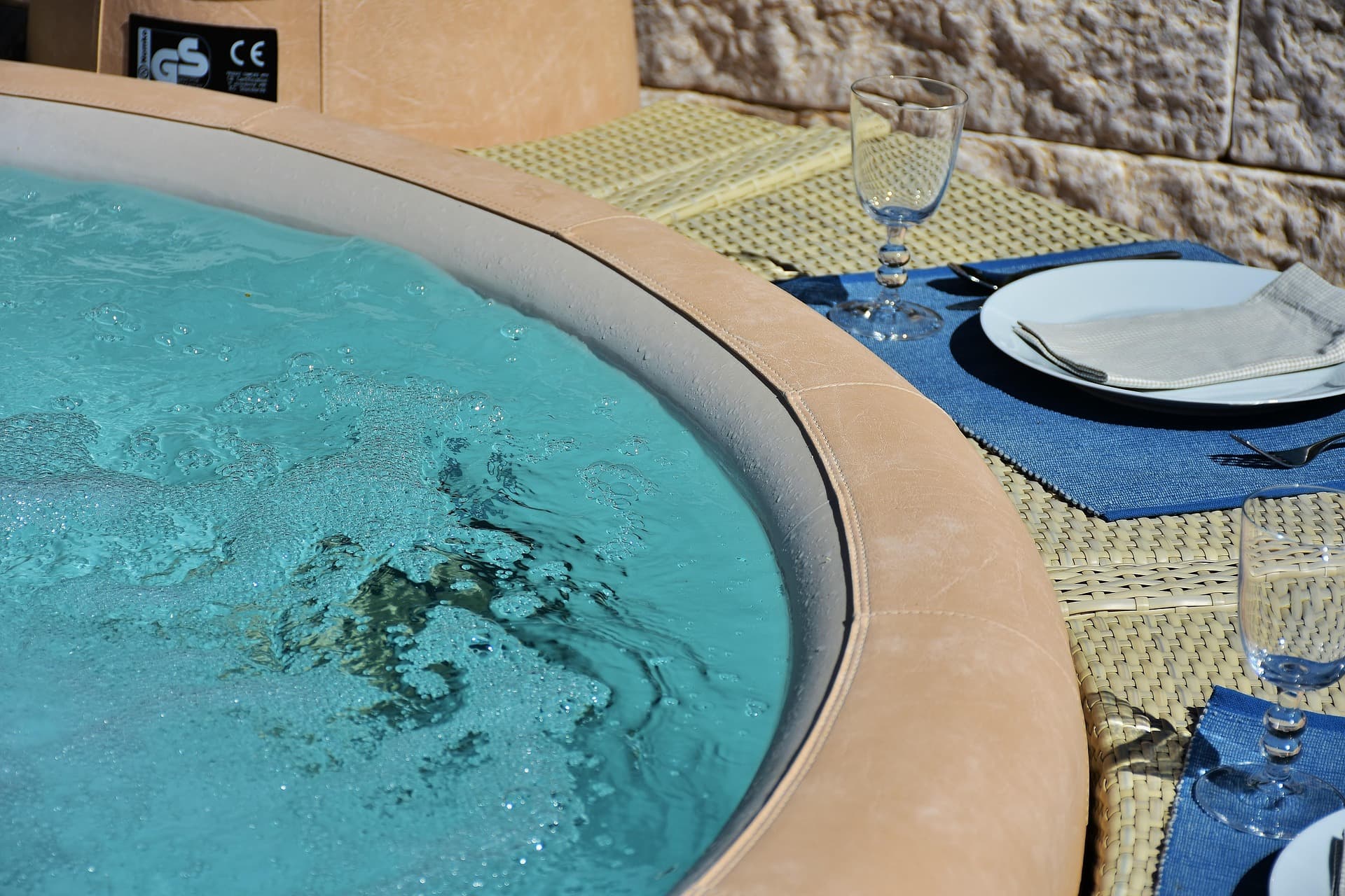 Spa en eau turquoise avec margelle, adossé à un mur de pierre